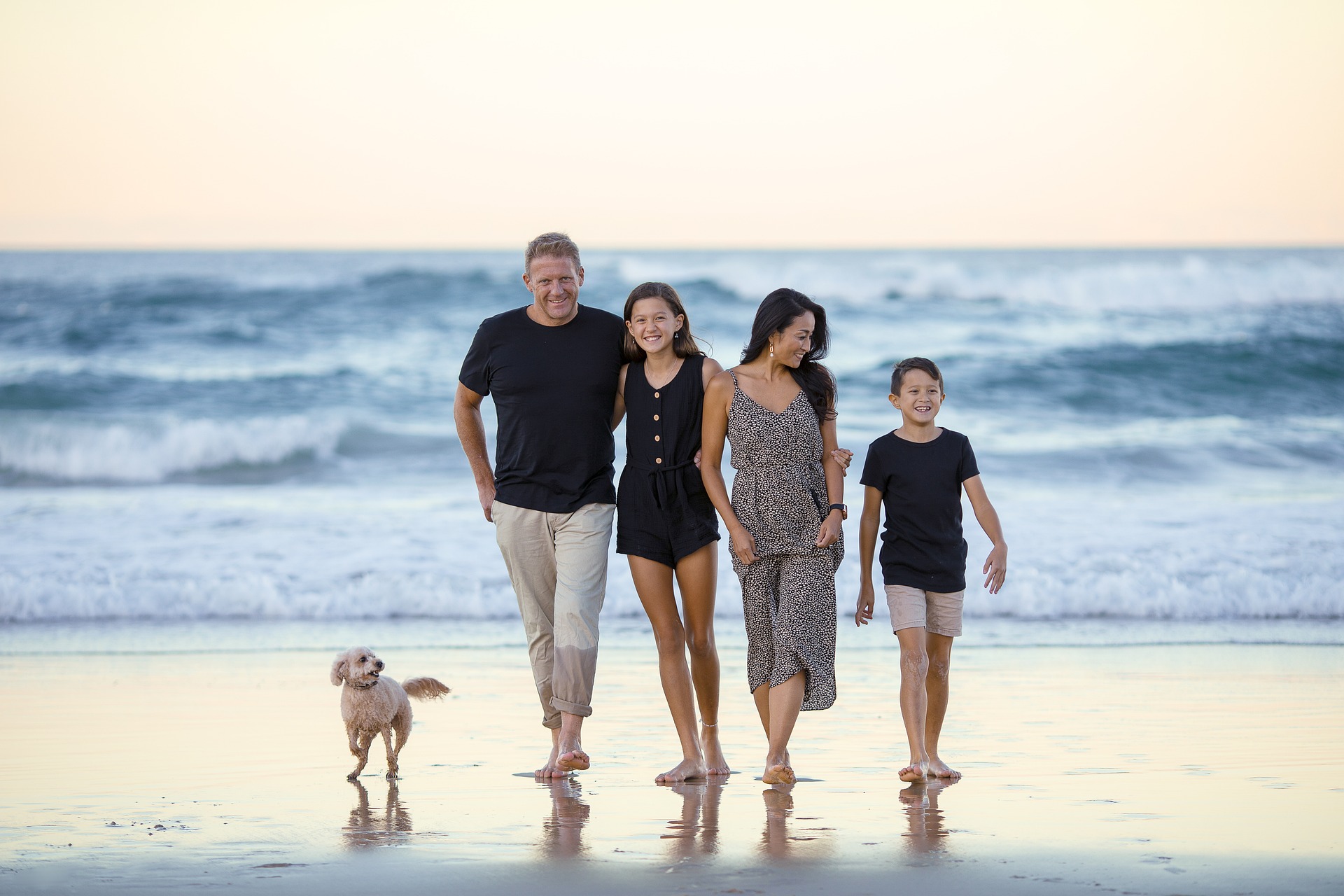 A family, father, mother, 2 children and a dog walking on the beach